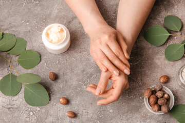 Female hands with jar of shea butter, nuts and leaves on grunge background