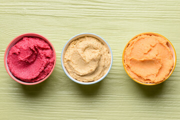 Bowls with tasty hummus on color wooden background