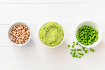 Bowls with tasty peas hummus and chickpeas on light wooden background