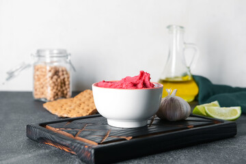 Bowl with tasty beet hummus and garlic on dark table, closeup