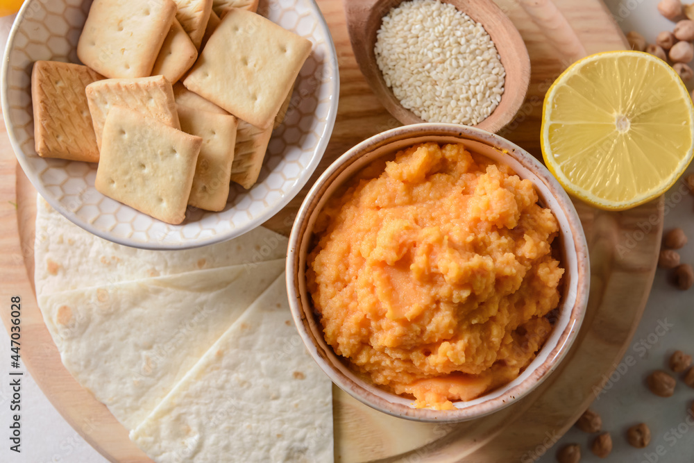 Wall mural Bowl with tasty carrot hummus, lemon and crackers on light background, closeup