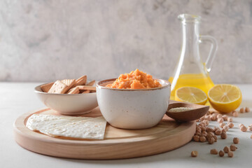 Bowl with tasty carrot hummus and crackers on light background