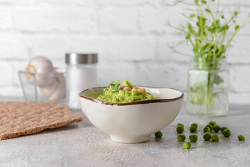 Bowl with tasty green pea hummus and crackers on light background