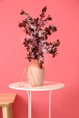 Vase with blooming branches on table in room