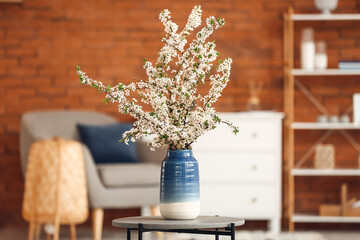 Vase with beautiful blossoming branches on table in room