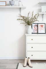 Vase with beautiful blossoming branches on chest of drawers in room