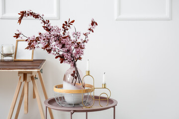 Vase with blossoming branches on table near light wall