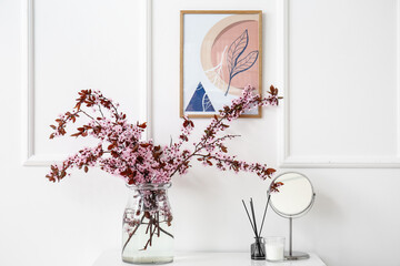 Vase with blossoming branches on shelf near light wall