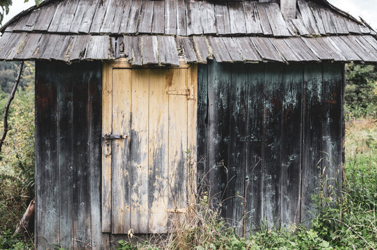 An old small Carpathian wooden house, blackened with age, with a traditional wooden tile roof. A yellow grunge door with peeling paint is closed with a rusty iron bolt with hinges made by a blacksmith