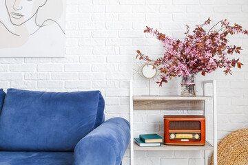 Book shelf and vase with blossoming branches near brick wall