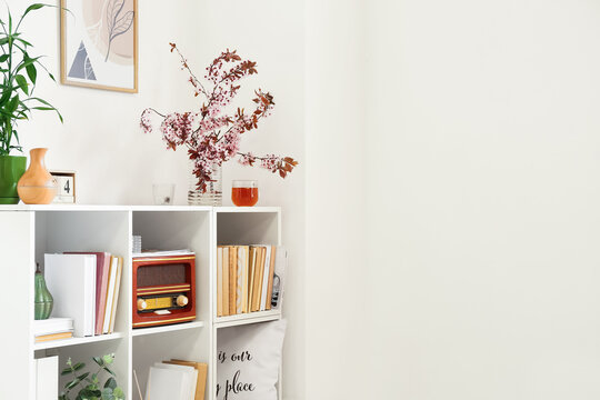 Shelf unit with blossoming branches and decor near light wall