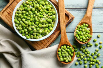 Spoons and bowl with frozen green peas on color wooden background