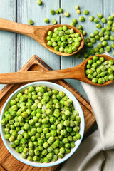 Spoons and bowl with frozen green peas on color wooden background