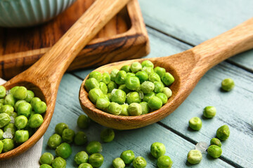 Spoons with frozen green peas on color wooden background