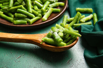 Spoon with frozen green beans on color background