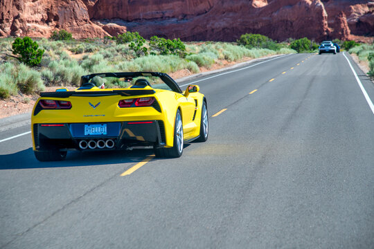 ARCHES NATIONAL PARK, UT - JULY 1, 2019: Yellow Corvette speeds up along a major park road in summer season.