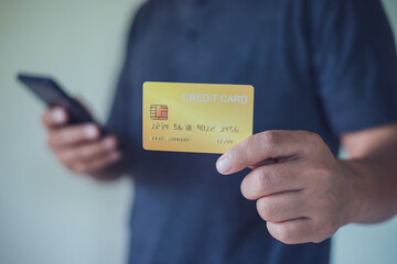 Man holding a credit card and using smart phone for online payment, using online banking application on his cell phone.
