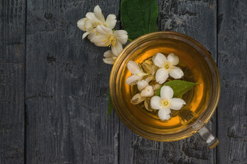 Glass cup with fresh floral tea and jasmine flowers on a wooden background.