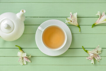 Fototapeta na wymiar Cup of floral tea, teapot and flowers on color wooden background