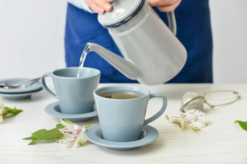 Woman pouring tea from teapot into cup on table
