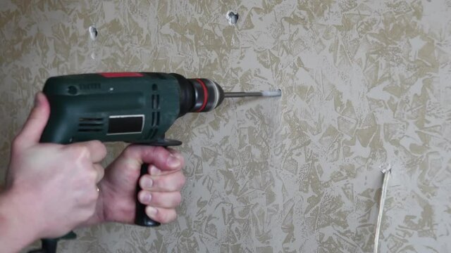 Man drills hole in marbled painted plaster wall. Male hands hold electric drill to make hole with twist drill bit rotating. DIY home improvement