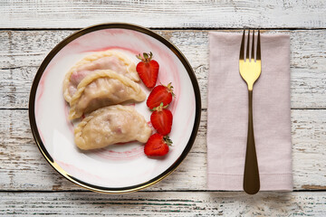 Plate with tasty strawberry dumplings  on light wooden background