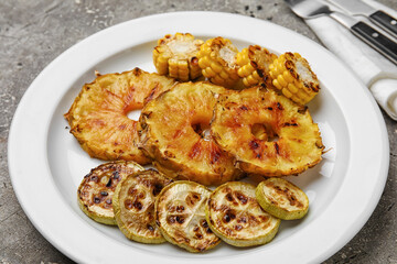 Plate with grilled pineapple slices and vegetables on grunge background, closeup