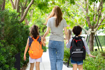 Parent and pupil of primary school go hand in hand. Woman and kids with backpack behind the back. Beginning of lessons.first day at school.Mother taking daughter to school