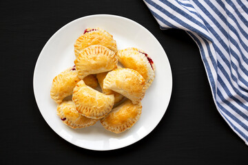 Homemade Cherry Hand Pies on a plate on a black surface, overhead view. Top view, from above, flat lay.