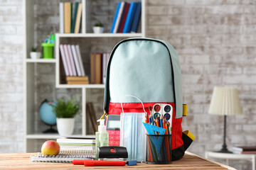 School backpack with stationery and medical mask on table in classroom