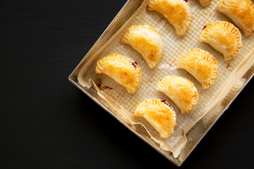 Homemade Cherry Hand Pies in a baking pan on a black background, top view. Space for text.