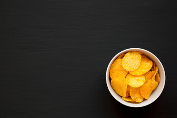 Ruffled Cheese Potato Chips in a Bowl on a black background, top view. Flat lay, overhead, from above. Copy space.