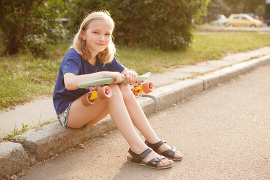 Lovely young girl smiling joyfully, resting after skating on her pennyboard, copy space