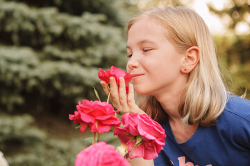 Close up of a lovely happy young girl smelling pink flowers and smiling with her eyes closed