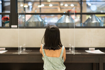 Back asian child or kid girl sitting alone between protection glass wall or clear plastic partition...