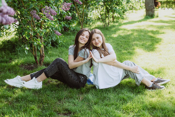 Two young happy teenage girls are resting in the park on the green grass. Female friendship. Soft selective focus.