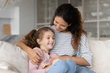 Fototapeta na wymiar Smiling young Latino mom and teen daughter relax on sofa at home have fun cuddling tickling. Happy Hispanic mother and teenage girl child rest on couch enjoy family lazy leisure weekend together.