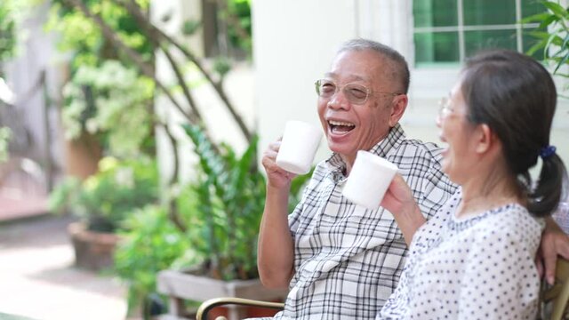 slow motion of senior asian couple husband and wife laughing while drinking coffee in morning at home garden. concept of family and togetherness