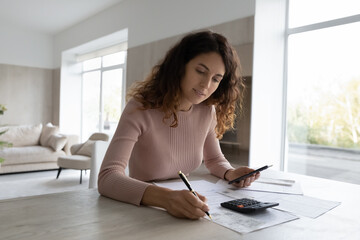 Young Latino woman sit at desk at home manage household expenses expenditure make payment online on...