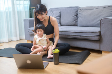 Happy young woman in sportswear is with daughter exercising in living room at home