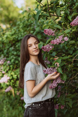 Beautiful young woman, teenager girl, near a lilac bush in a sunny spring park. Soft selective focus.