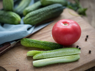 Sliced and whole cucumbers .  Cucumber and tomato on a cutting board .  Vegetables salad. Dieting. Vegetarian food.   