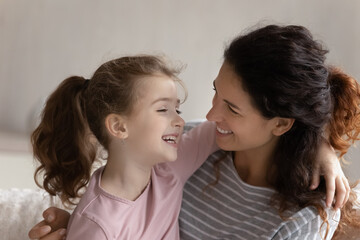 Smiling young Hispanic mother and small teen daughter hug laugh playing together at home. Overjoyed...