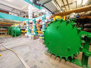 Green heat exchanger in an industrial cellar. Lots of pipes and pumps.