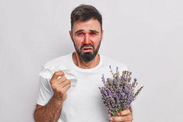 Puzzled unhappy bearded adult man has runny nose holds handkerchief cannot stop sneezing has...