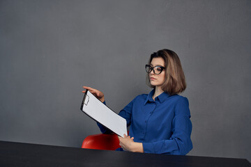 a woman in a blue shirt sits at the table a folder in her hands documents