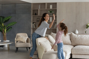 Overjoyed young Latino mother and little teen daughter give high five for well-done house work....