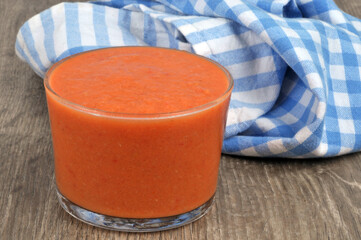 Verre de gaspacho avec un torchon à carreaux au second plan en gros plan sur un fond en bois