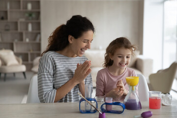 Smiling loving Hispanic mom and teen daughter have fun make experiments play lab game at home together. Happy caring Latino mother and small girl child engaged in chemistry laboratory activity.