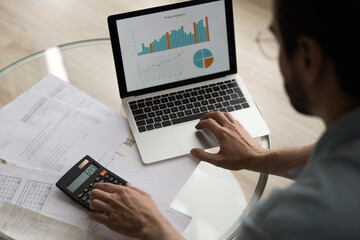 Close up above view man sit at table verifies data, financial report with graphs and charts...